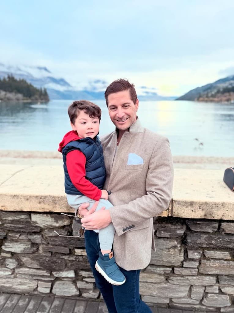 Parry holding his young child beside a lake, with mountains behind them